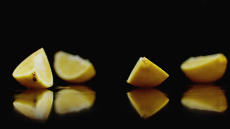 Juicy-sliced-​​yellow-lemon-fall-into-4-parts-glass-with-water-splashes-in-slow-motion-on-a-dark-background
